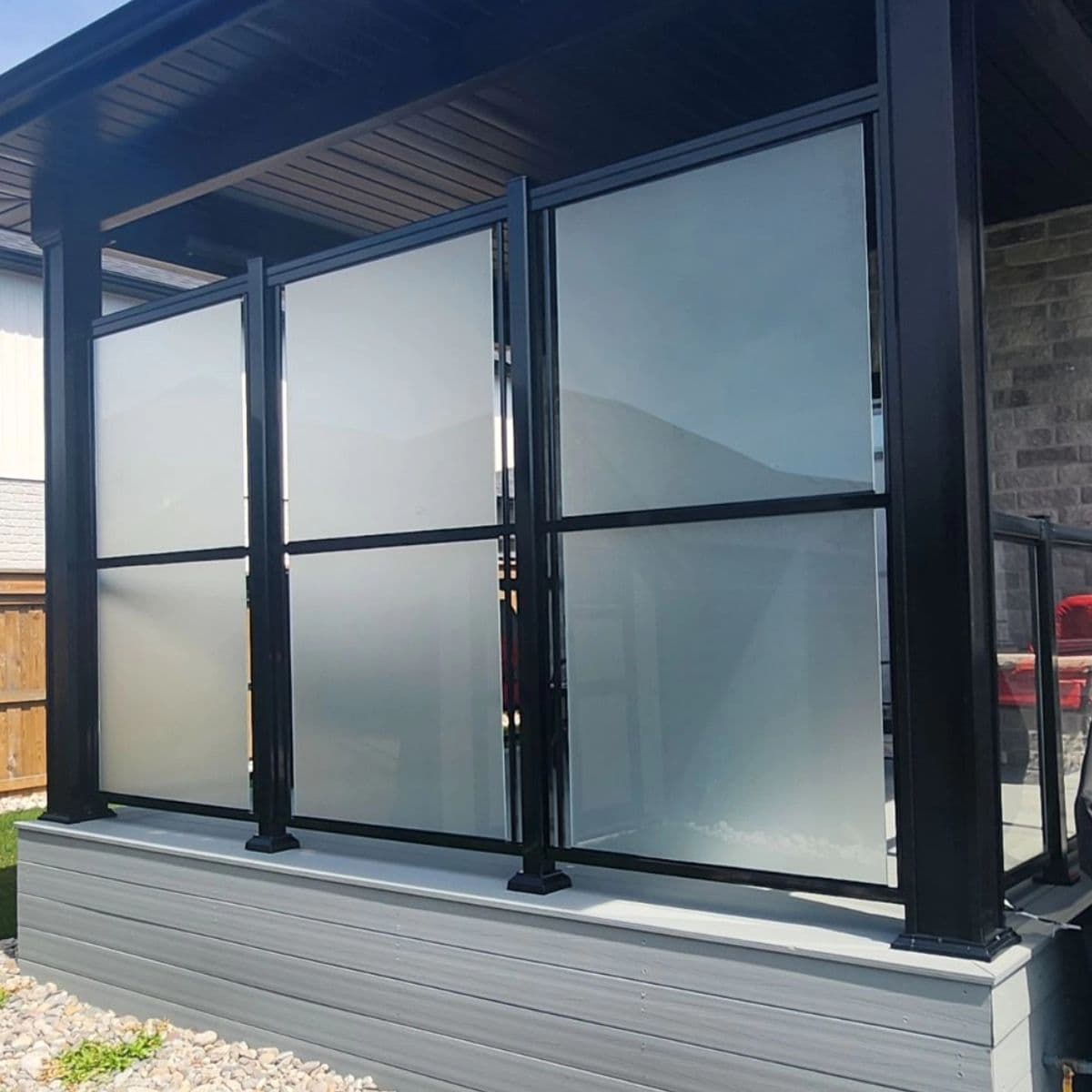 Modern frosted glass privacy screen with black metal frames on a light gray outdoor deck.