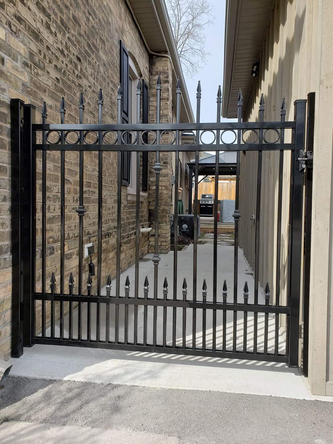 Black metal gate with pointed finials and circular designs between two residential walls.