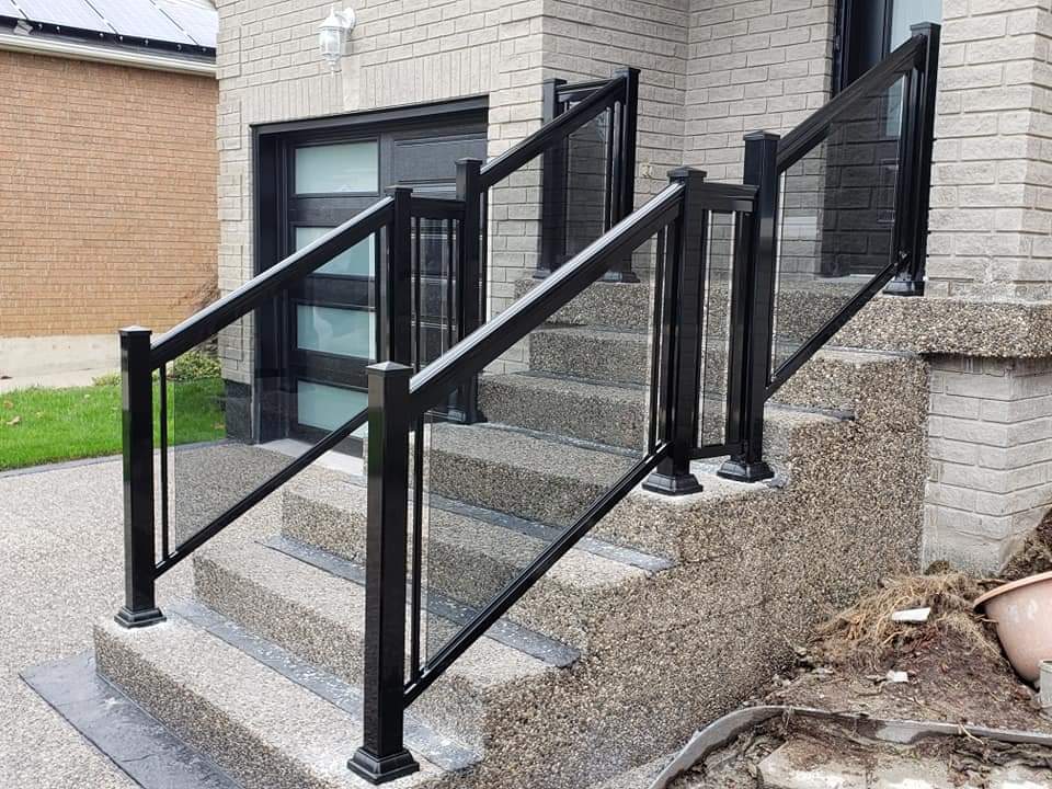 Modern black metal and glass railings on textured concrete stairs leading to a brick house.
