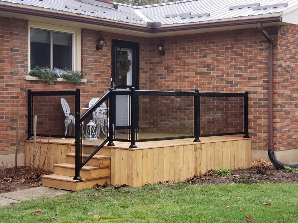 Small wooden deck with black metal and glass railings attached to a red brick house.