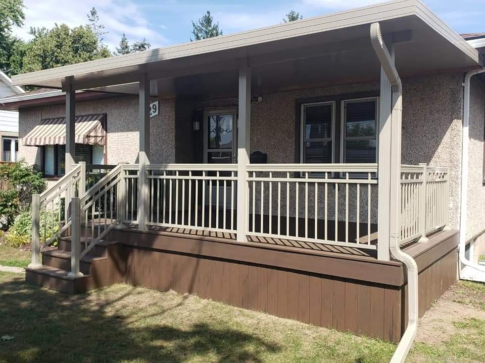 A covered front porch featuring tan railings, brown base, and a flat roof overhang.