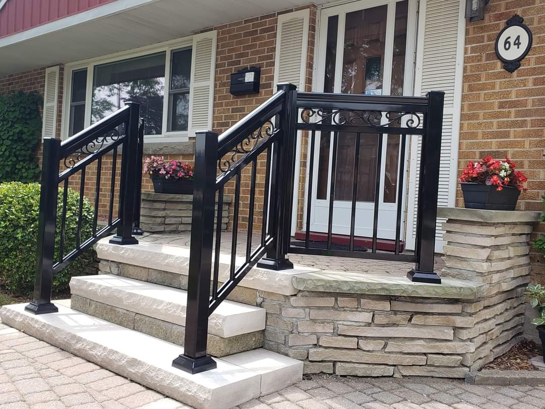Black metal railings with decorative scrollwork on stone steps leading to a brick house entrance.