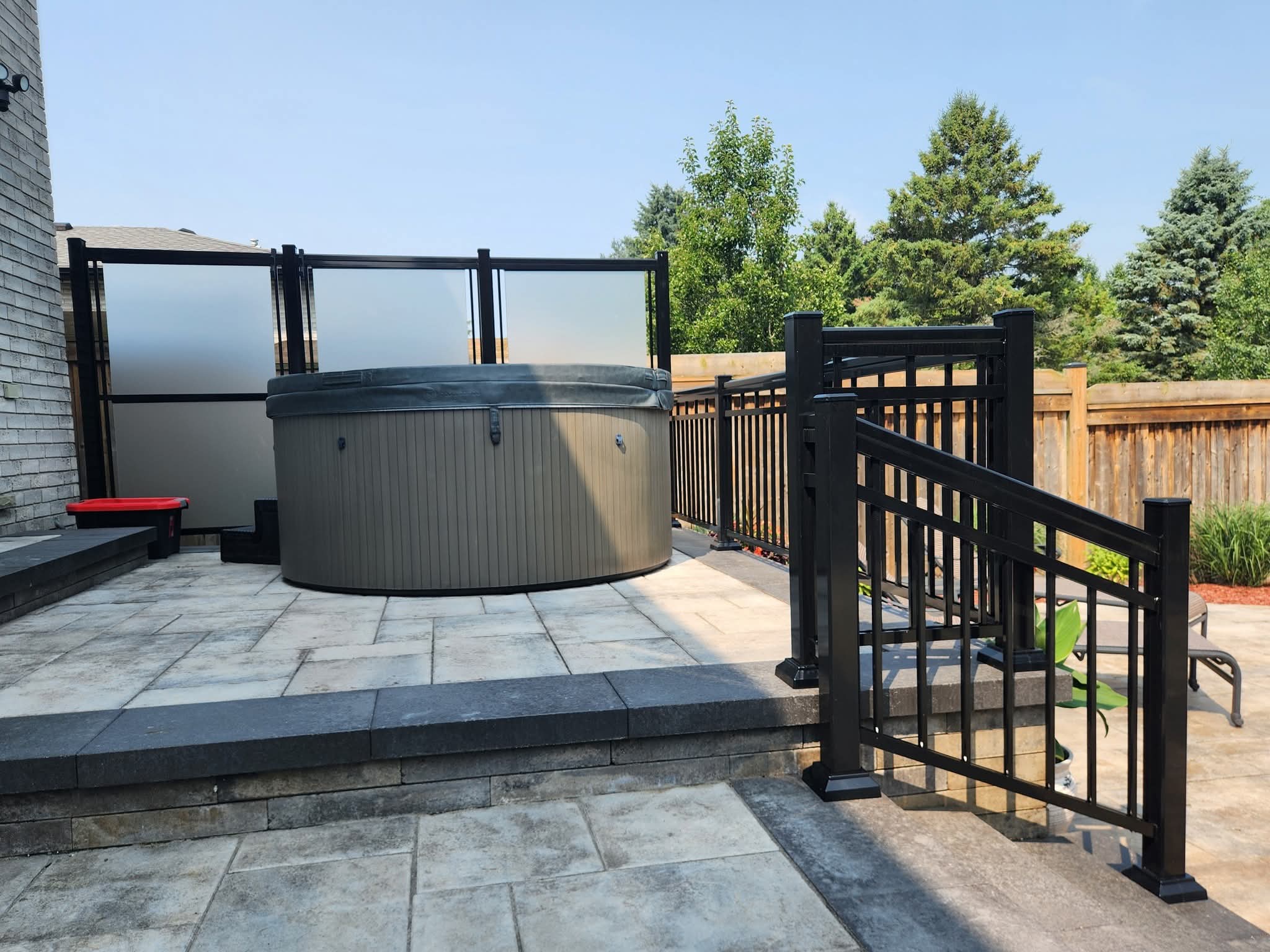 Covered round hot tub on a stone patio with black railings and frosted privacy screens.