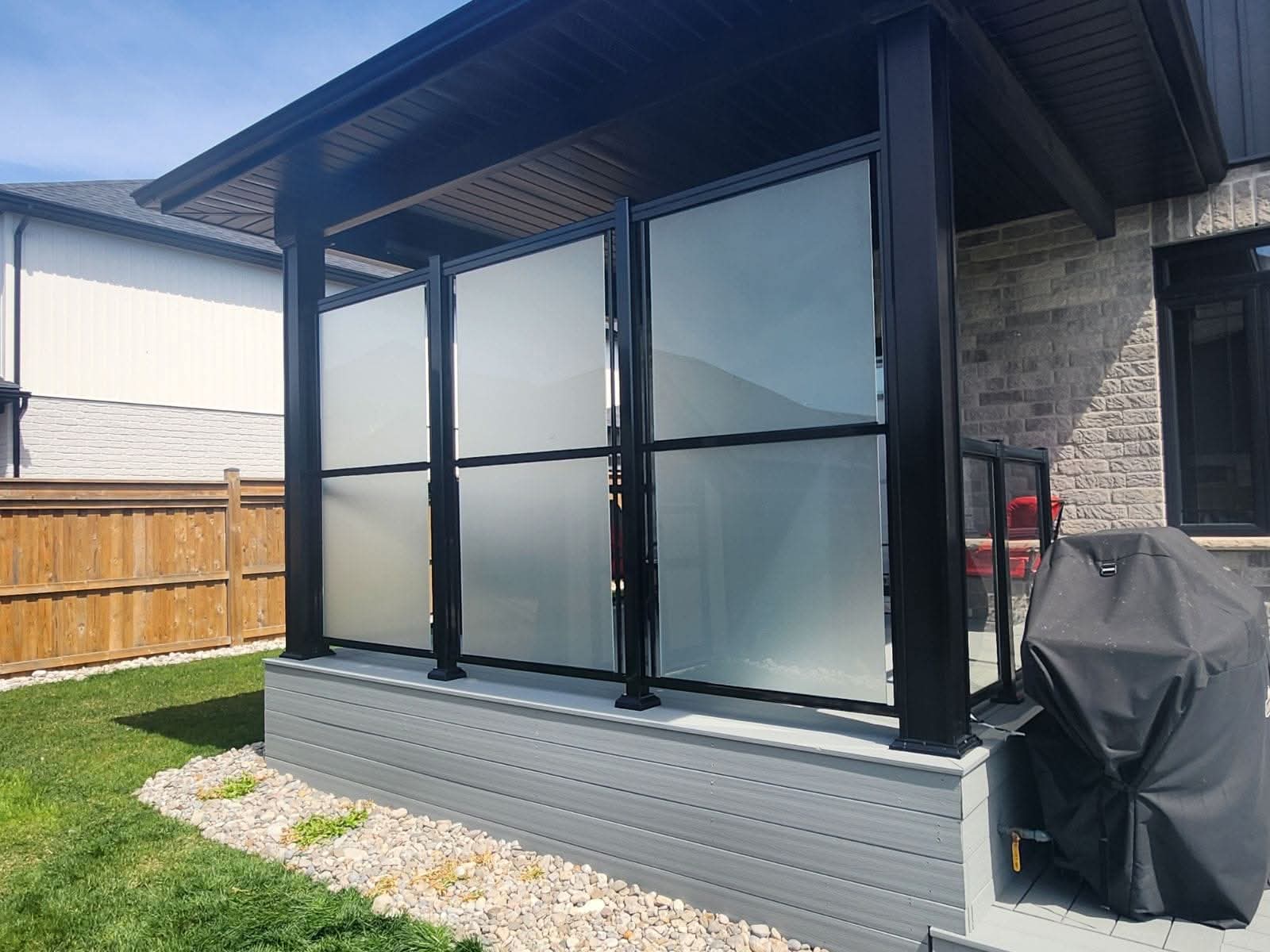 Frosted glass privacy screens with black frames on a gray deck under a dark covered roof.