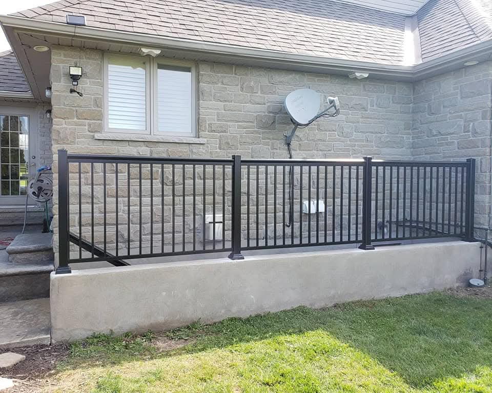 Black metal railing on a concrete wall outside a stone house with a green lawn.