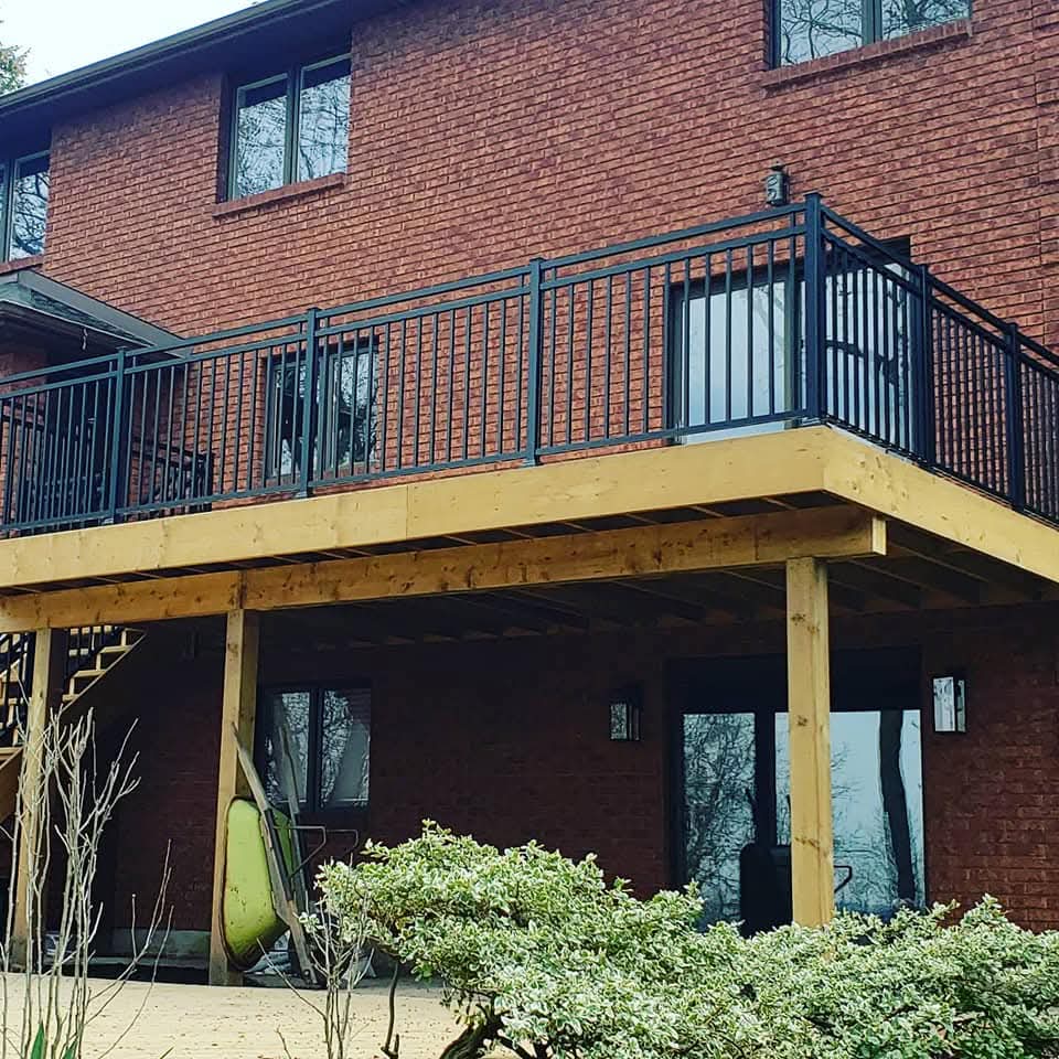 Elevated wooden deck with black metal railings on a two-story red brick house.