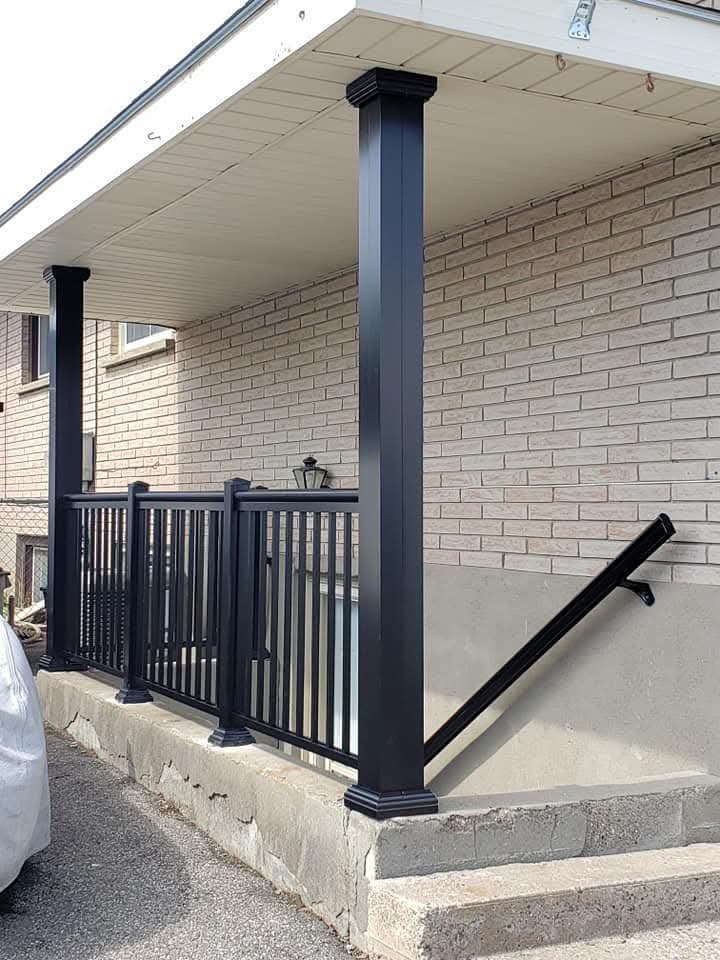 Modern black metal railings and support columns installed on a concrete porch with brick siding.