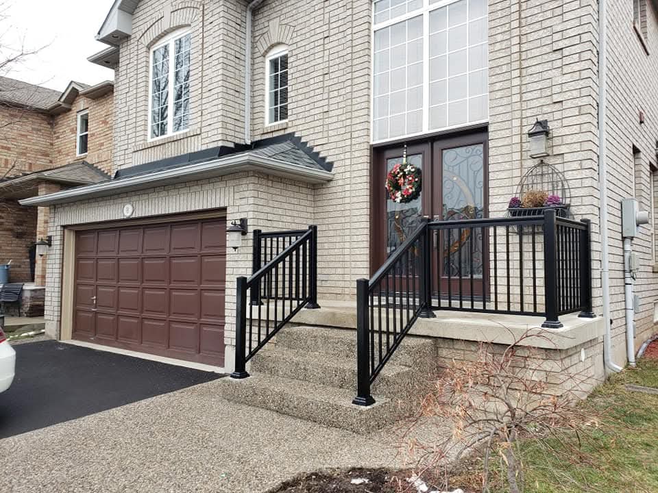 Brick house with black metal railings on concrete steps leading to a brown double door.