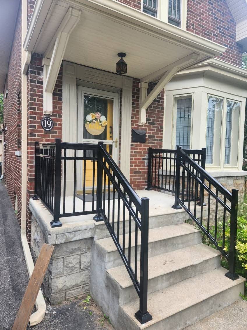 Concrete steps with black metal railings leading to a brick house's yellow front door.