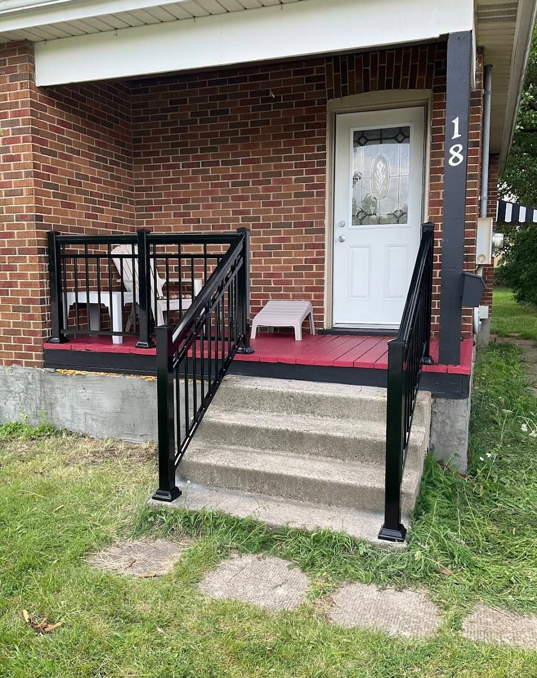 Concrete steps with black railings lead to a red porch and white front door.