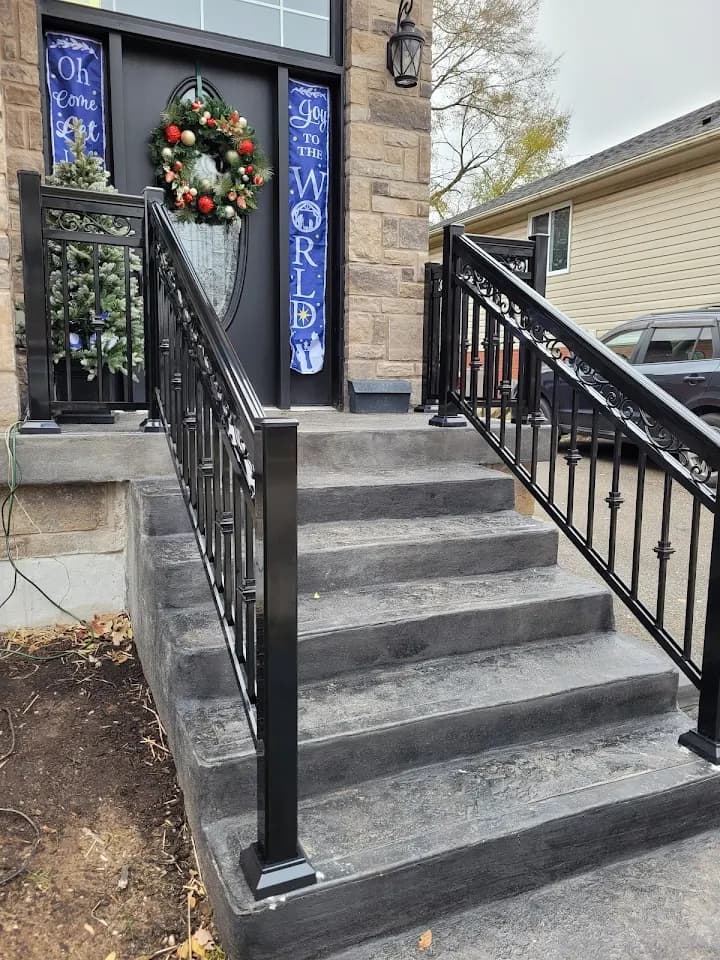 Concrete stairs with black metal railings lead to a front door decorated for Christmas.