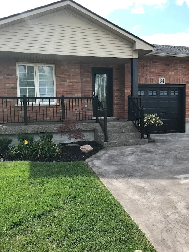 Brick home featuring black railings, a front porch, concrete steps, and a black garage door.