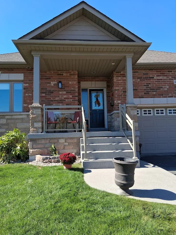 Brick house entrance featuring concrete steps, glass porch railings, and a black front door.